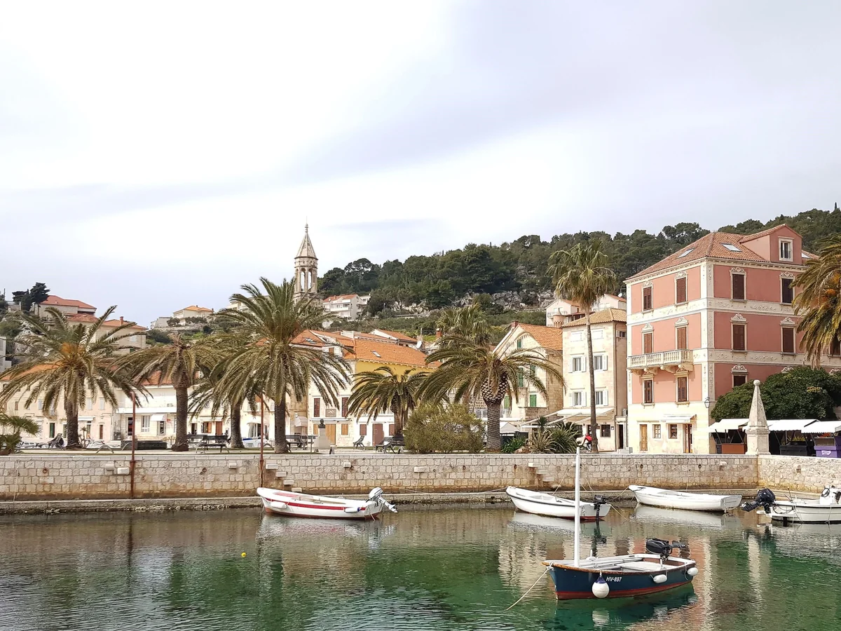 Hvar town's waterfront with palm trees, small moored boats and historic stone buildings